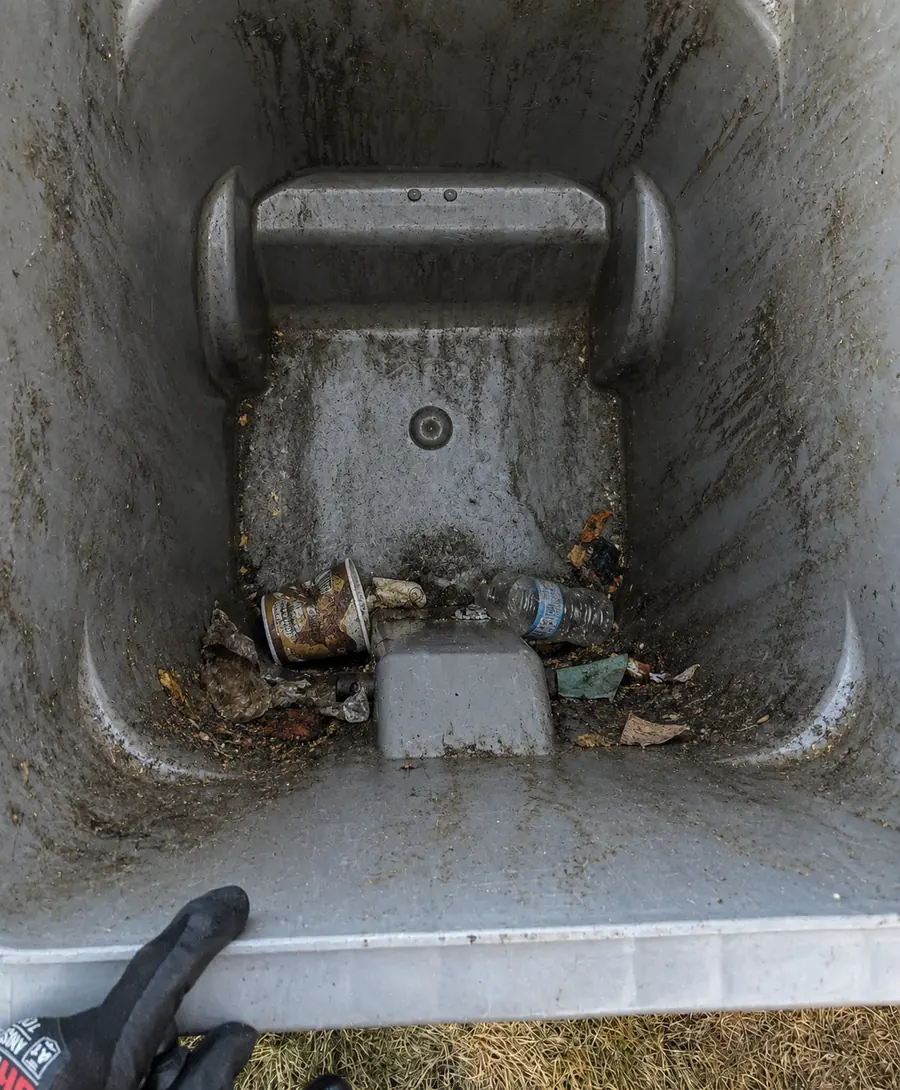 Inside of a garbage bin before cleaning, caked with grime and trash