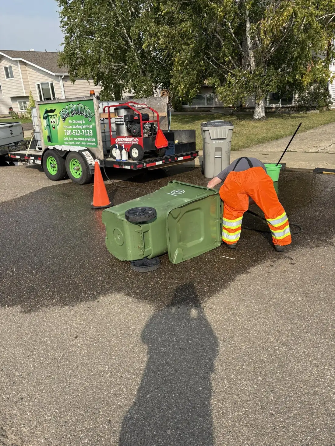 Bin Buddy crew member pressure washing a green bin at the curb